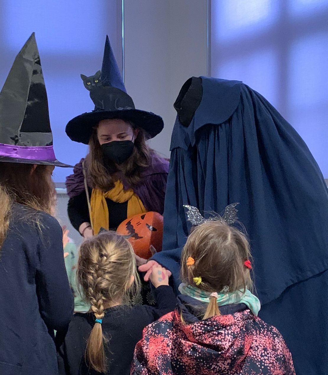 Die Kinder bekommen von einer als kopflosen Reiter verkleideten Person Süßigkeiten. Daneben steht eine als Hexe verkleidete Museumsführerin.