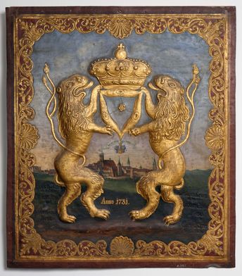 Museum Bautzen Das Meisterschild eines Tucmachers mit zwei reliefartig hervorgehobenen, goldenen Löwen, die eine goldene Krone tragen. Im Hintergrund ist Bautzen und blauer Himmel gemalt. Das Schild ist von einem goldenen Stuckrahmen umgeben.