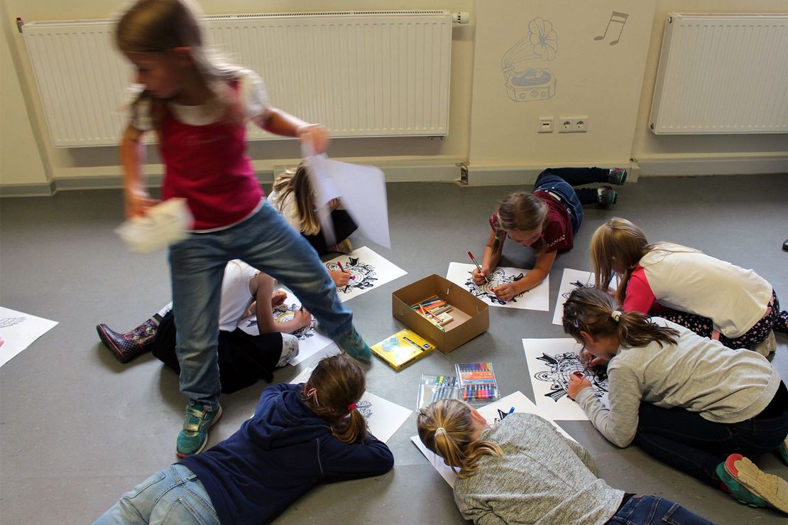 Fünf Kinder liegen auf dem Fußboden und malen 