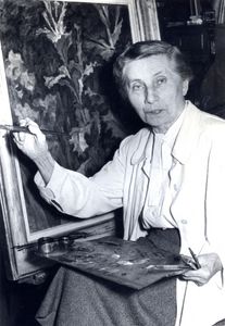 schwarz-weiß Aufnahmen- eine Frau sitzt mit Farbpalette auf dem Schoß und Pinsel in der Hand vor ihrem Gemälde