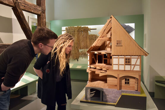 Eine Frau und ein Mann sehen sich die verkleinerte Rekonstruktion eines Umgebindehauses an.