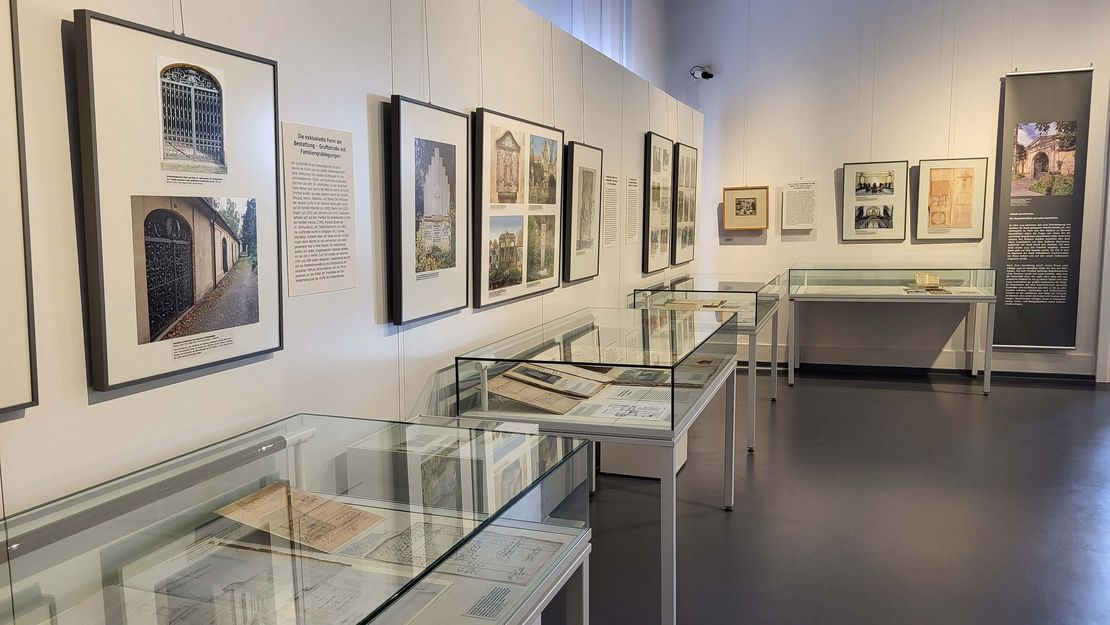 Foto der Kabinettausstellung zum Taucherfriedhof. Zu sehen sind zwei Wände mit Bildern und Vitrinen mit Ausstellungsstücken.